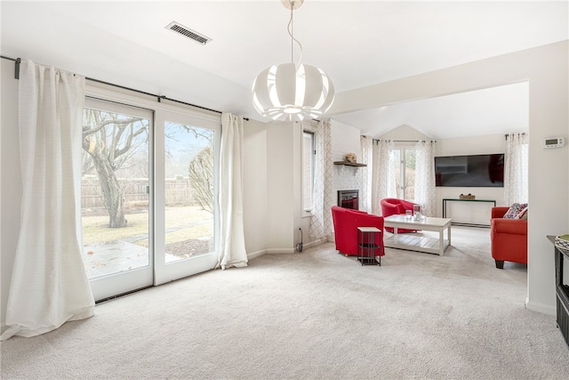 living area featuring visible vents, carpet, a brick fireplace, and a chandelier