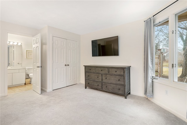 bedroom with a closet, baseboards, light colored carpet, and ensuite bath