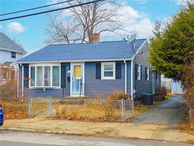 view of front of property with a shingled roof, central AC, a chimney, and a fenced front yard