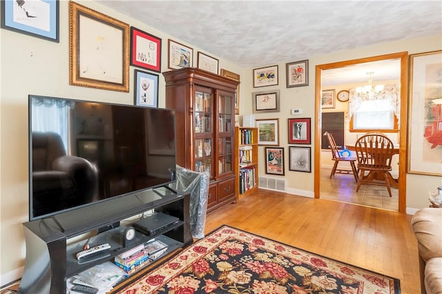 interior space with a notable chandelier, visible vents, a textured ceiling, wood finished floors, and baseboards