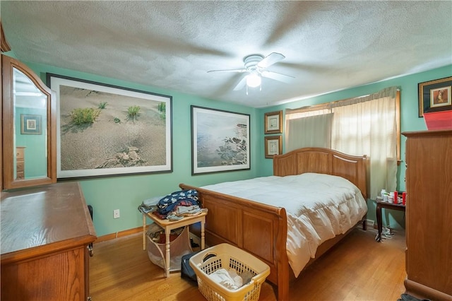 bedroom featuring a textured ceiling, ceiling fan, light wood-style flooring, and baseboards