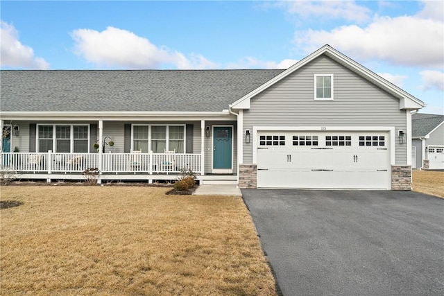 view of front of house with roof with shingles, a porch, stone siding, driveway, and a front lawn