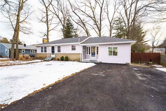 ranch-style house with driveway, a chimney, and fence