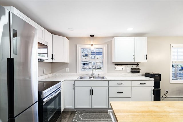 kitchen featuring stainless steel appliances, hanging light fixtures, white cabinets, a sink, and wood finished floors