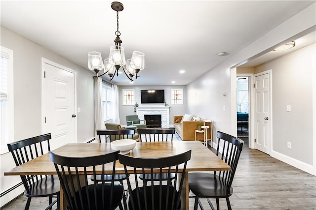 dining space with baseboards, wood finished floors, an inviting chandelier, a fireplace, and a baseboard heating unit