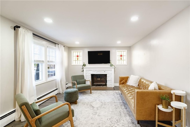 living area with a stone fireplace, a baseboard radiator, wood finished floors, and recessed lighting