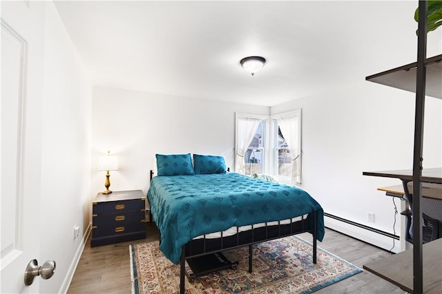 bedroom with baseboards, a baseboard heating unit, and wood finished floors