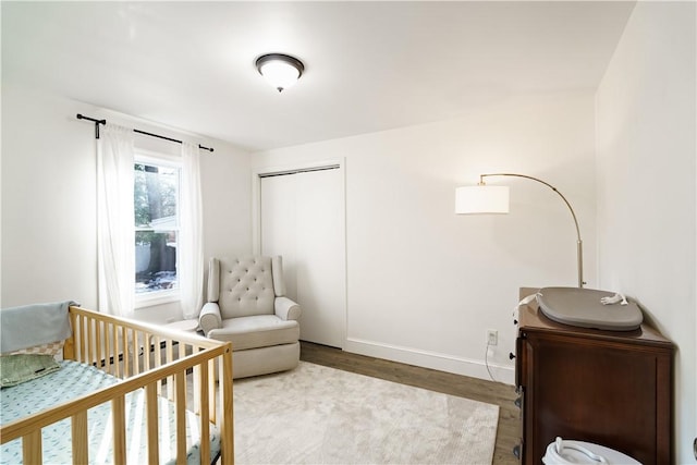 bedroom with a crib, a closet, wood finished floors, and baseboards