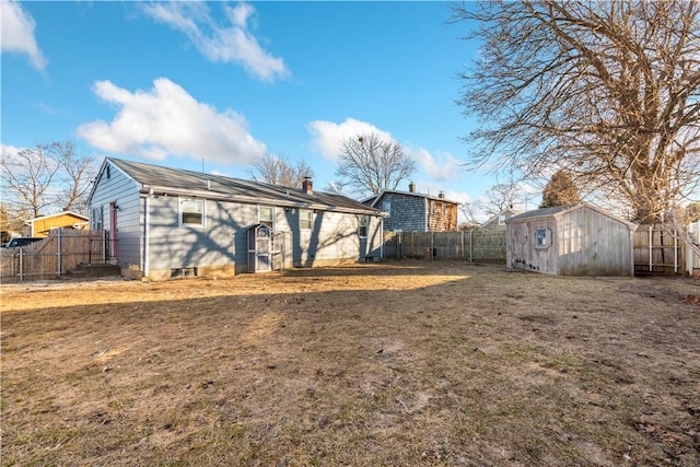 back of property featuring an outbuilding, a fenced backyard, a yard, a storage unit, and a chimney