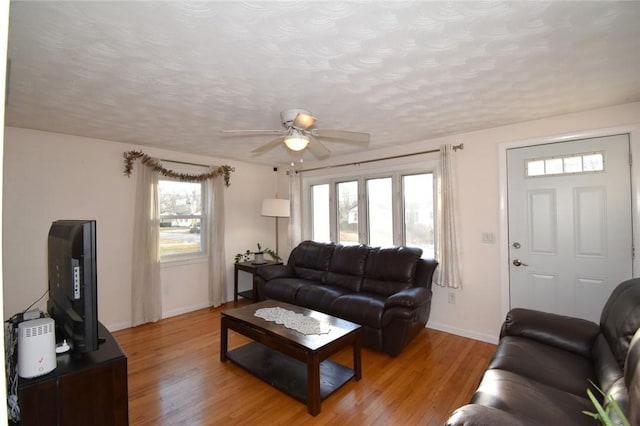 living room with a textured ceiling, light wood-type flooring, a wealth of natural light, and baseboards