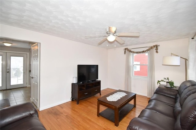 living area with light wood finished floors, french doors, a textured ceiling, and baseboards