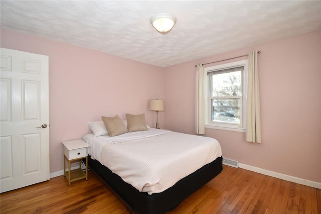 bedroom featuring baseboards, a textured ceiling, visible vents, and hardwood / wood-style floors