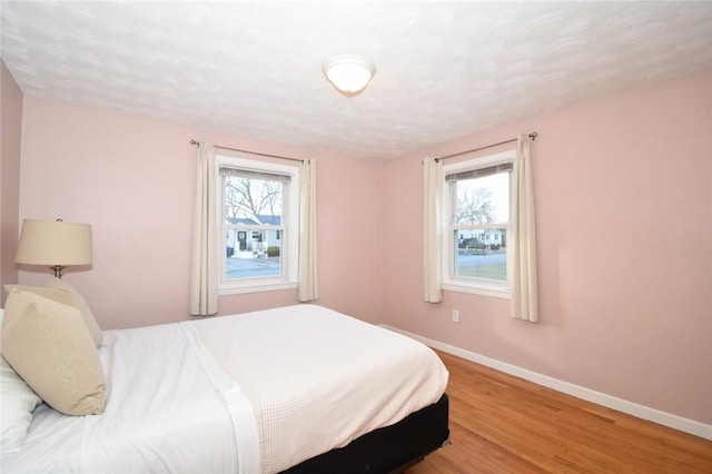 bedroom with multiple windows, baseboards, and wood finished floors