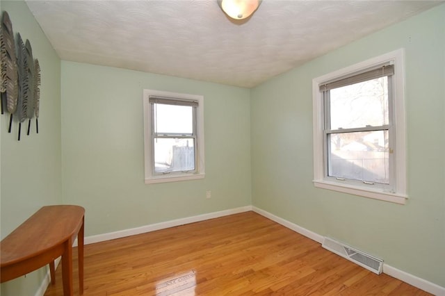 unfurnished room featuring light wood-style floors, visible vents, and baseboards