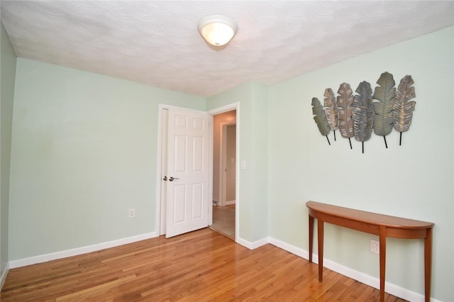 spare room with light wood-style floors, a textured ceiling, and baseboards