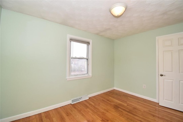 spare room with baseboards, visible vents, light wood-style flooring, and a textured ceiling