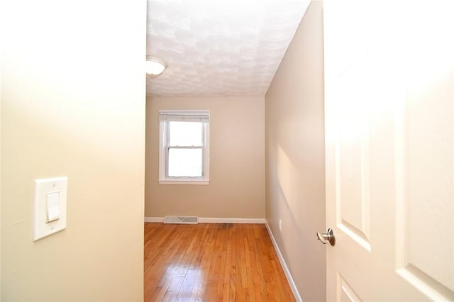 empty room with a textured ceiling, light wood-style flooring, visible vents, and baseboards