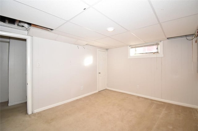 below grade area featuring light carpet, a drop ceiling, and baseboards