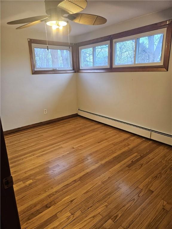 spare room featuring a baseboard heating unit, baseboards, ceiling fan, and hardwood / wood-style floors