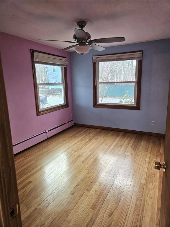 spare room with ceiling fan, a baseboard radiator, baseboards, and wood-type flooring