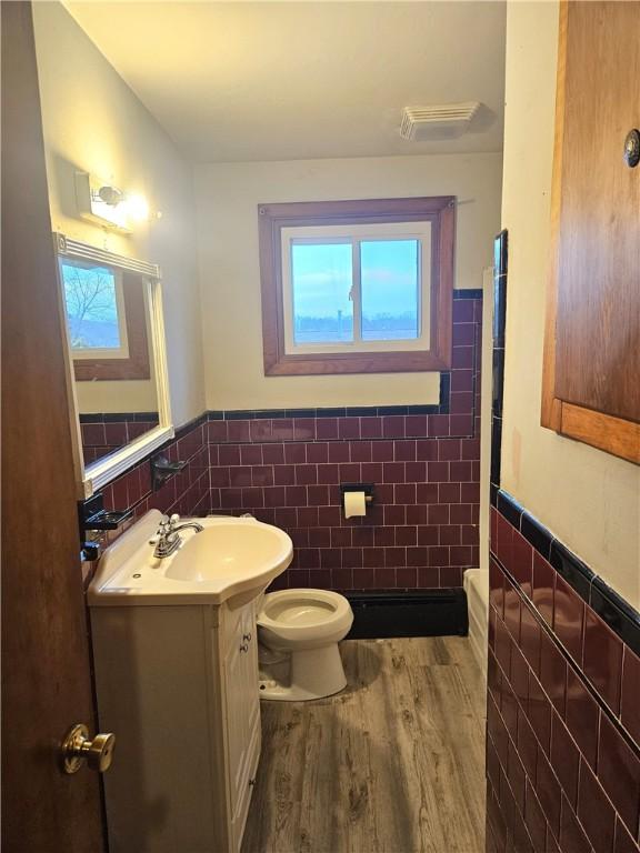 bathroom featuring a wainscoted wall, tile walls, toilet, vanity, and wood finished floors