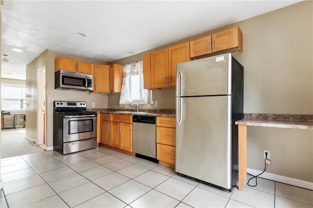 kitchen featuring light tile patterned floors, appliances with stainless steel finishes, a sink, and baseboards