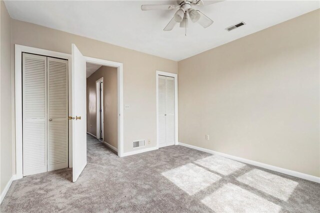 unfurnished bedroom featuring baseboards, visible vents, two closets, and light colored carpet