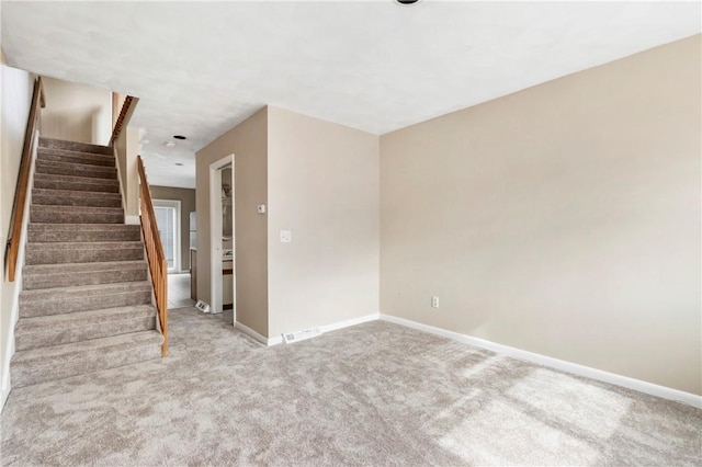 carpeted spare room with visible vents, stairway, and baseboards