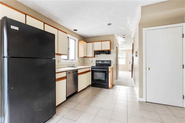 kitchen with light tile patterned flooring, under cabinet range hood, a sink, light countertops, and black appliances