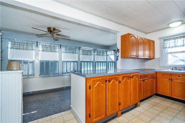 kitchen with a peninsula, a sink, a ceiling fan, brown cabinets, and light floors