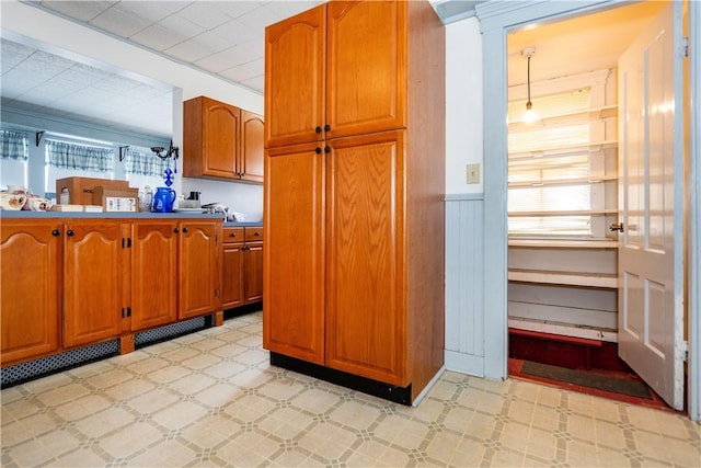 kitchen featuring light floors, visible vents, brown cabinetry, and wainscoting