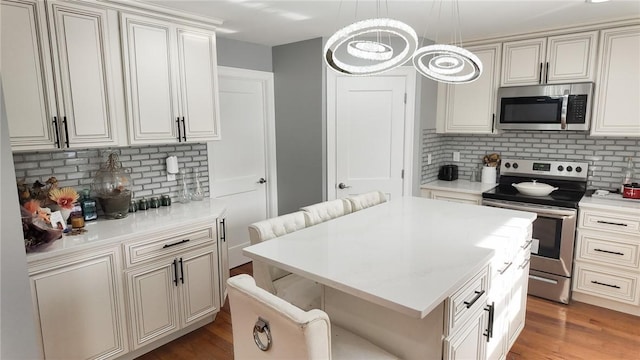 kitchen featuring stainless steel appliances, wood finished floors, a kitchen island, light countertops, and decorative backsplash