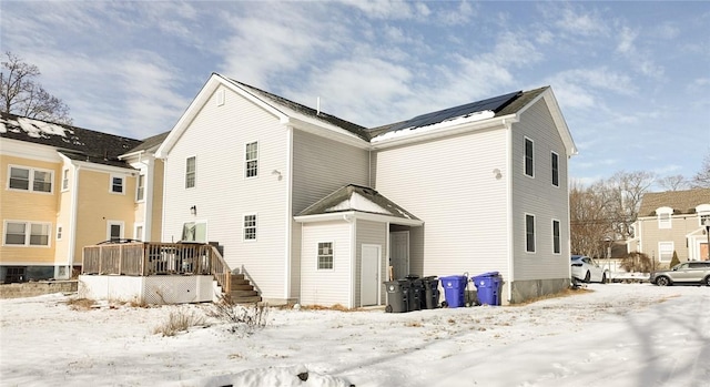 snow covered rear of property featuring solar panels and a wooden deck