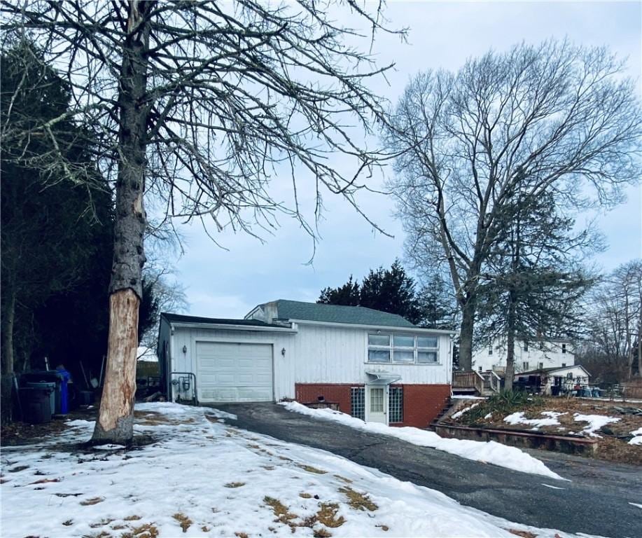 view of snow covered exterior featuring a garage, driveway, and brick siding