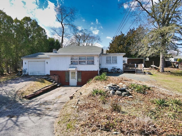 view of front of property with driveway, a wooden deck, a garage, and brick siding