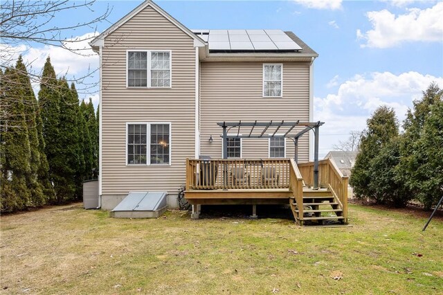 rear view of property featuring a deck, a yard, roof mounted solar panels, and a pergola