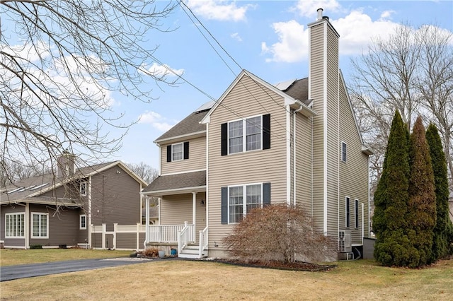 view of front of home with roof with shingles, a front lawn, a chimney, and a porch