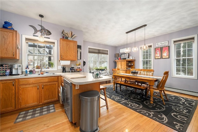 kitchen featuring a peninsula, a sink, light countertops, light wood-type flooring, and brown cabinetry