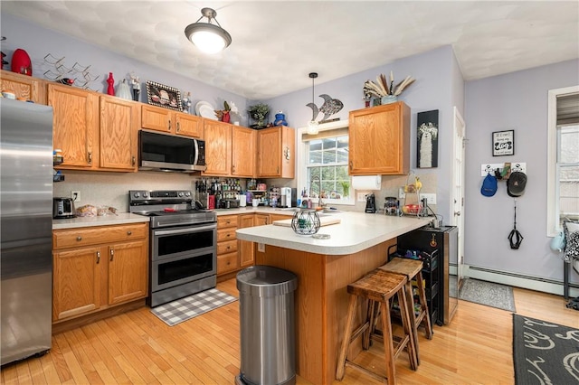 kitchen featuring appliances with stainless steel finishes, a peninsula, light countertops, a kitchen bar, and a baseboard heating unit