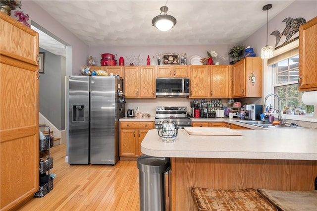 kitchen with stainless steel appliances, a peninsula, a sink, light wood-style floors, and light countertops