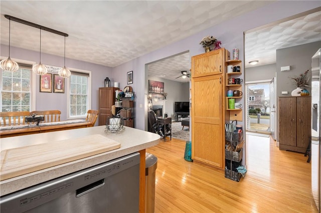 kitchen with light wood-style flooring, hanging light fixtures, light countertops, a fireplace, and stainless steel dishwasher