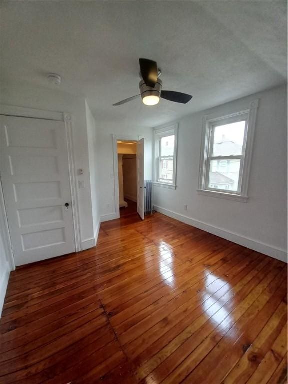 unfurnished bedroom featuring ceiling fan, radiator, hardwood / wood-style floors, and baseboards