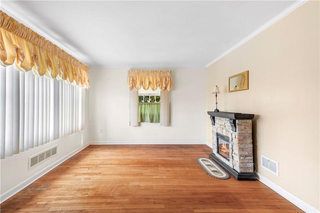 unfurnished living room featuring a stone fireplace, wood finished floors, visible vents, and crown molding