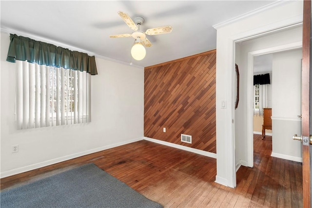 spare room featuring wooden walls, an accent wall, visible vents, wood-type flooring, and crown molding