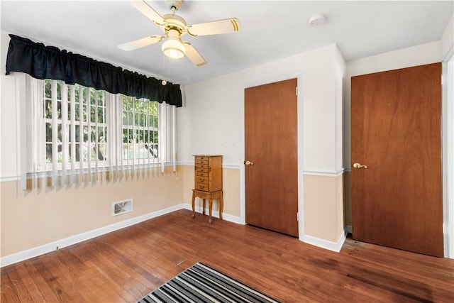 unfurnished bedroom featuring a ceiling fan, visible vents, baseboards, and wood finished floors