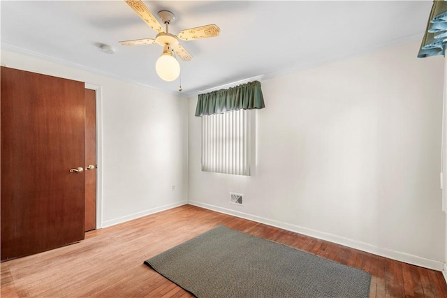 spare room with baseboards, visible vents, a ceiling fan, wood finished floors, and crown molding