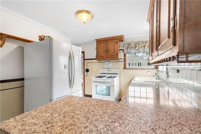 kitchen featuring white appliances, tile walls, brown cabinetry, and a sink