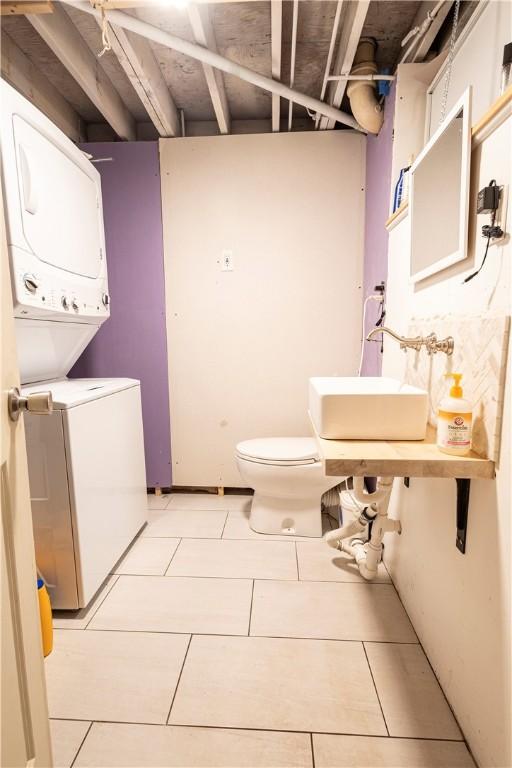 bathroom with toilet, stacked washer and dryer, tile patterned flooring, and a sink