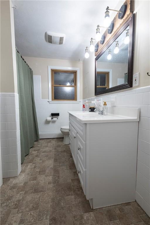 bathroom featuring visible vents, toilet, a wainscoted wall, vanity, and tile walls