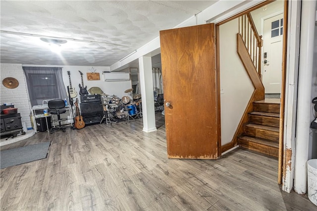 finished below grade area featuring a wood stove, stairs, wood finished floors, and an AC wall unit